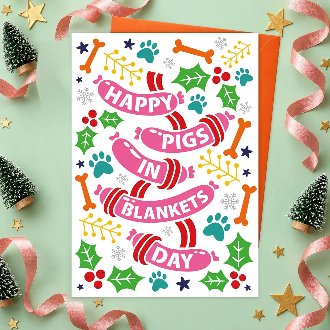 Pigs in Blankets Day – Edible Dog Christmas Card, bacon flavour by Scoff Paper, shown with an orange envelope